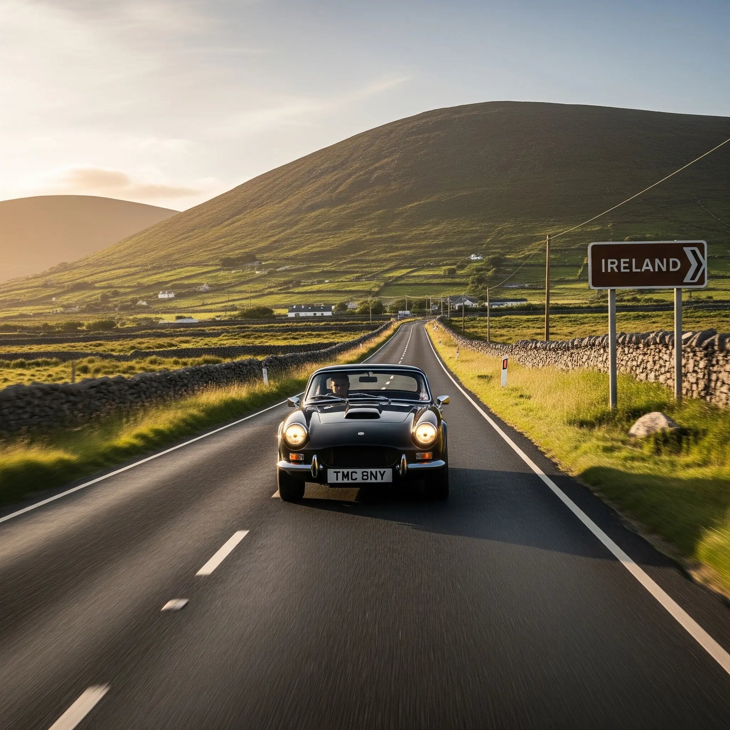 A TMC Costin driving down a long, straight road in the Irish countryside, with rolling green hills and stone walls in the background.