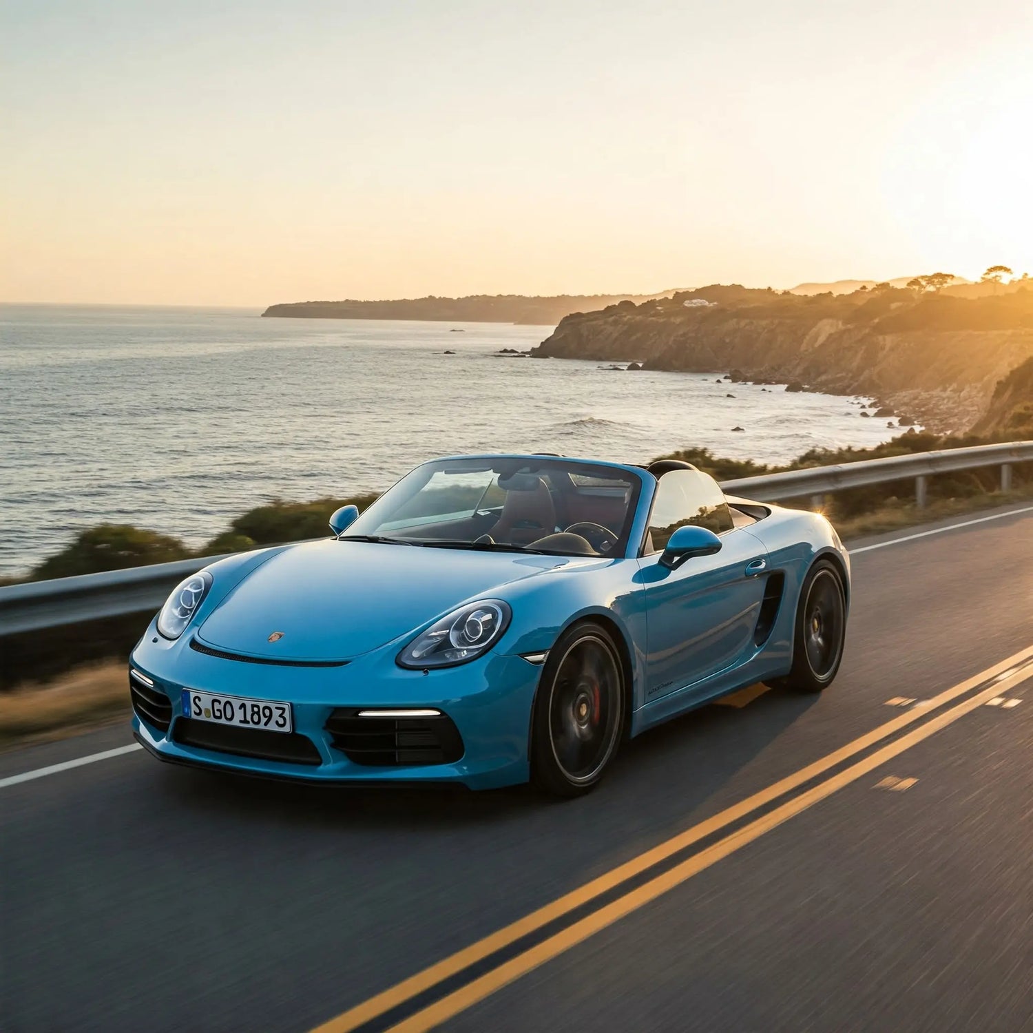 A bright blue Porsche 718 Spyder driving along a scenic coastal highway at sunset with ocean cliffs in the background.